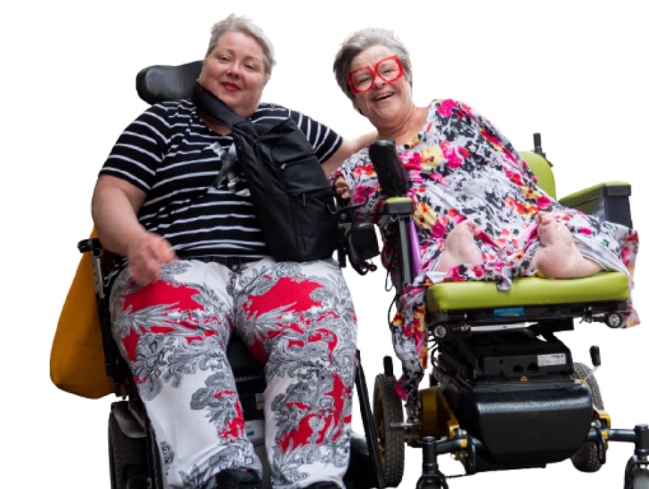 Two women in wheelchair and colourful clothing leaning towards each other and smiling to the camera.