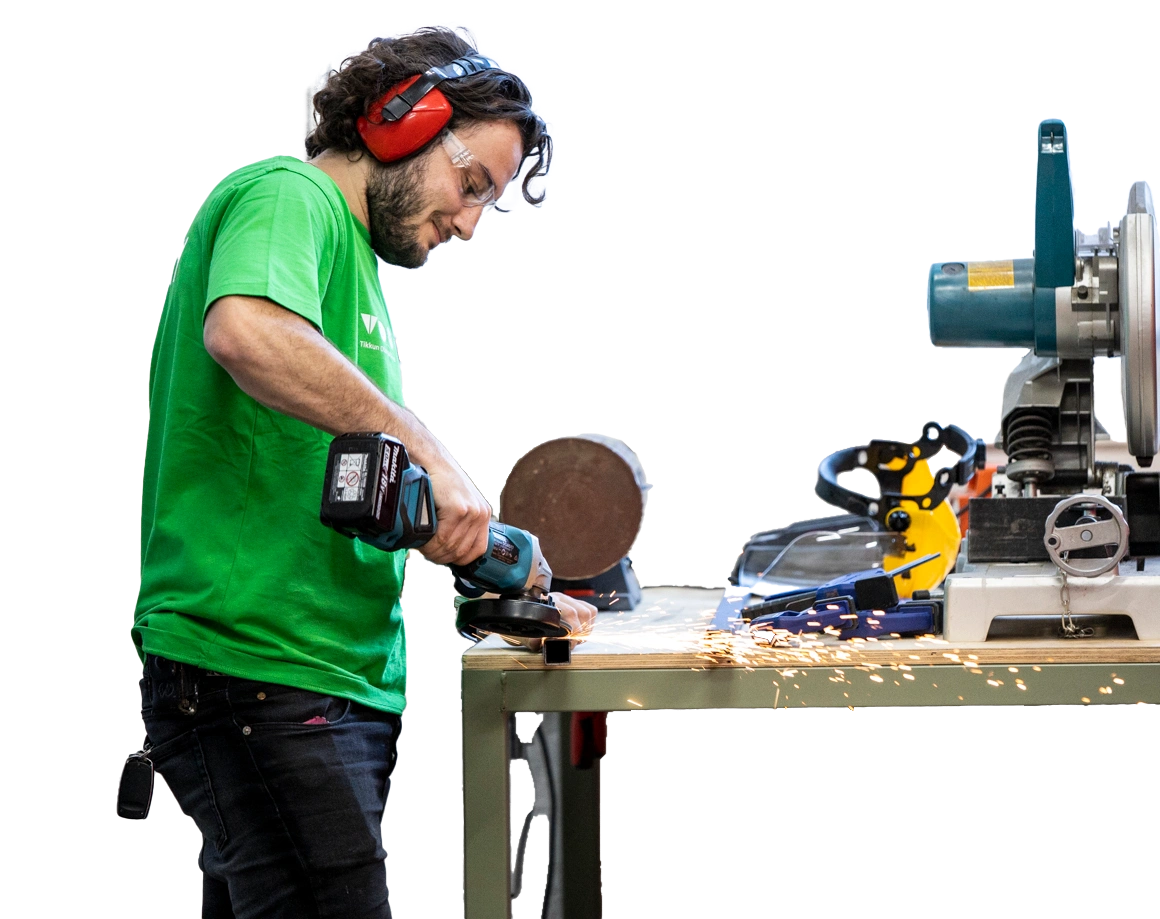 Man in green t-shirt using power tool by a work bench.
