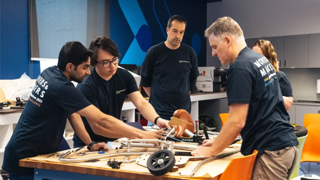 Five people standing around a white tricycle on a workbench.