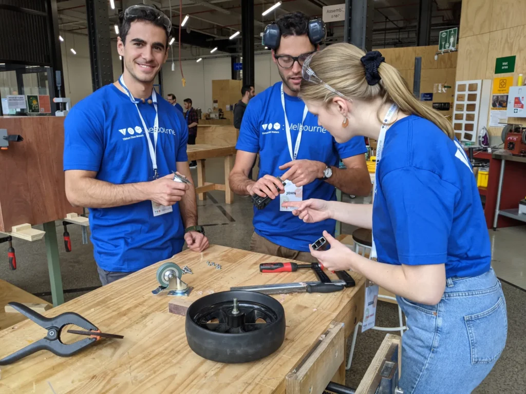 Three people standing around a work bench working on a wheel.