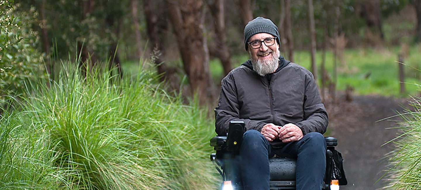 Man in wheelchair in the woods smiling to the camera.