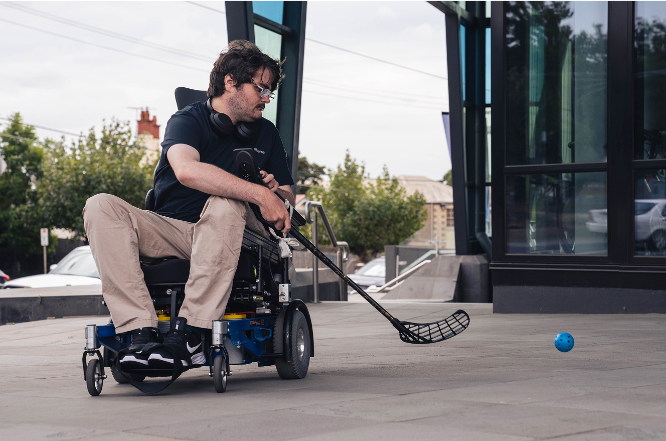 Man in wheelchair playing hockey outdoors.