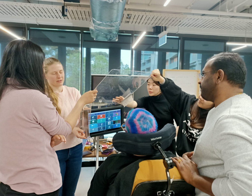 Man with blue and pink hair is watching a group of people fit a cover to his communication device.