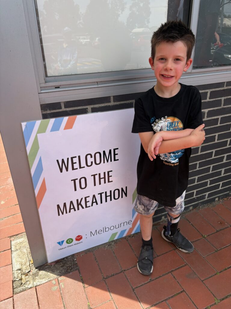 Boy standing in front of a sign saying "Welcome to the Makeathon" and smiling to the camera.