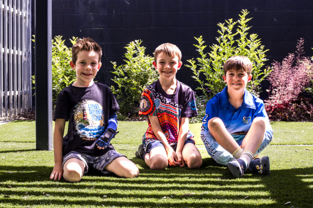 Three boys sitting on grass smiling to the camera.