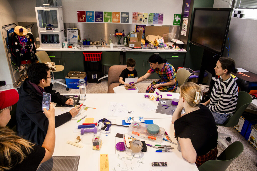 Four people are watching while a boy and his mum are testing a paper prototype.