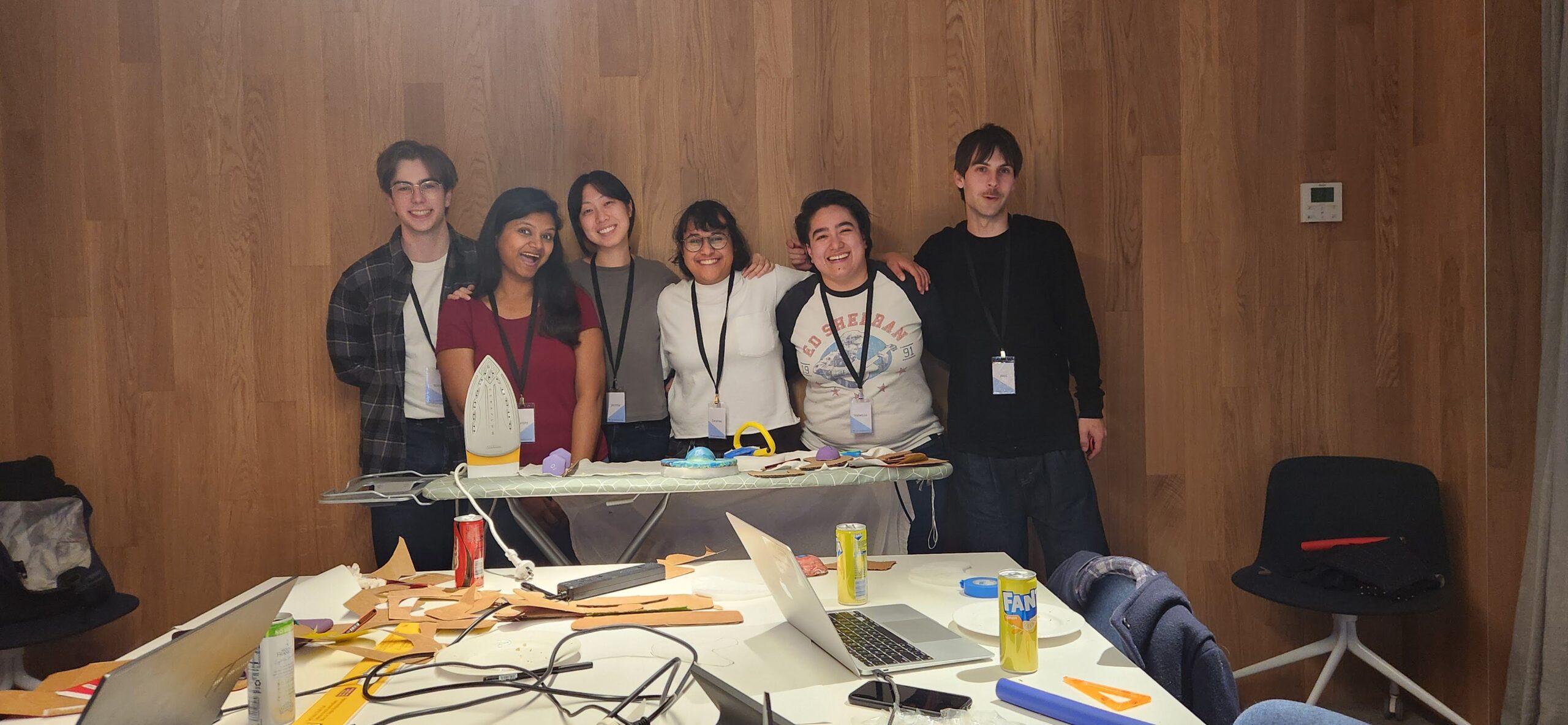 A group of 6 volunteers smiling to the camera from behind an ironing board. 