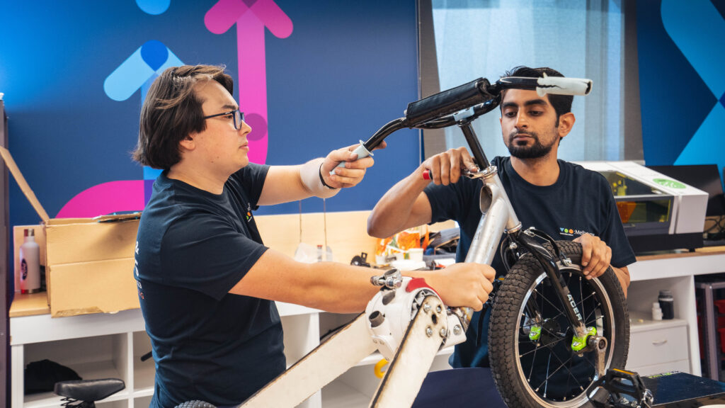 Two people holding up and working on a white tricycle.