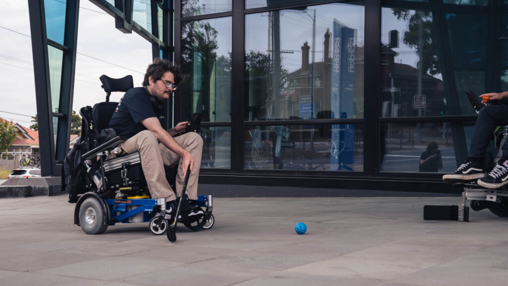 Man in power chair speeding towards a hocket ball with stick ready.