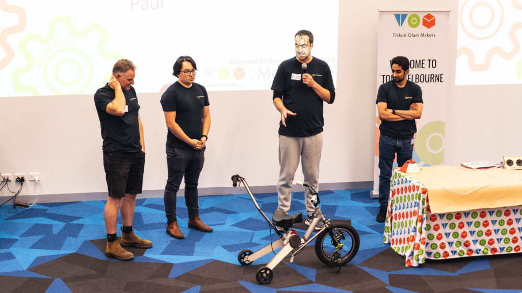 Four people in stage watching a modified kids bike.