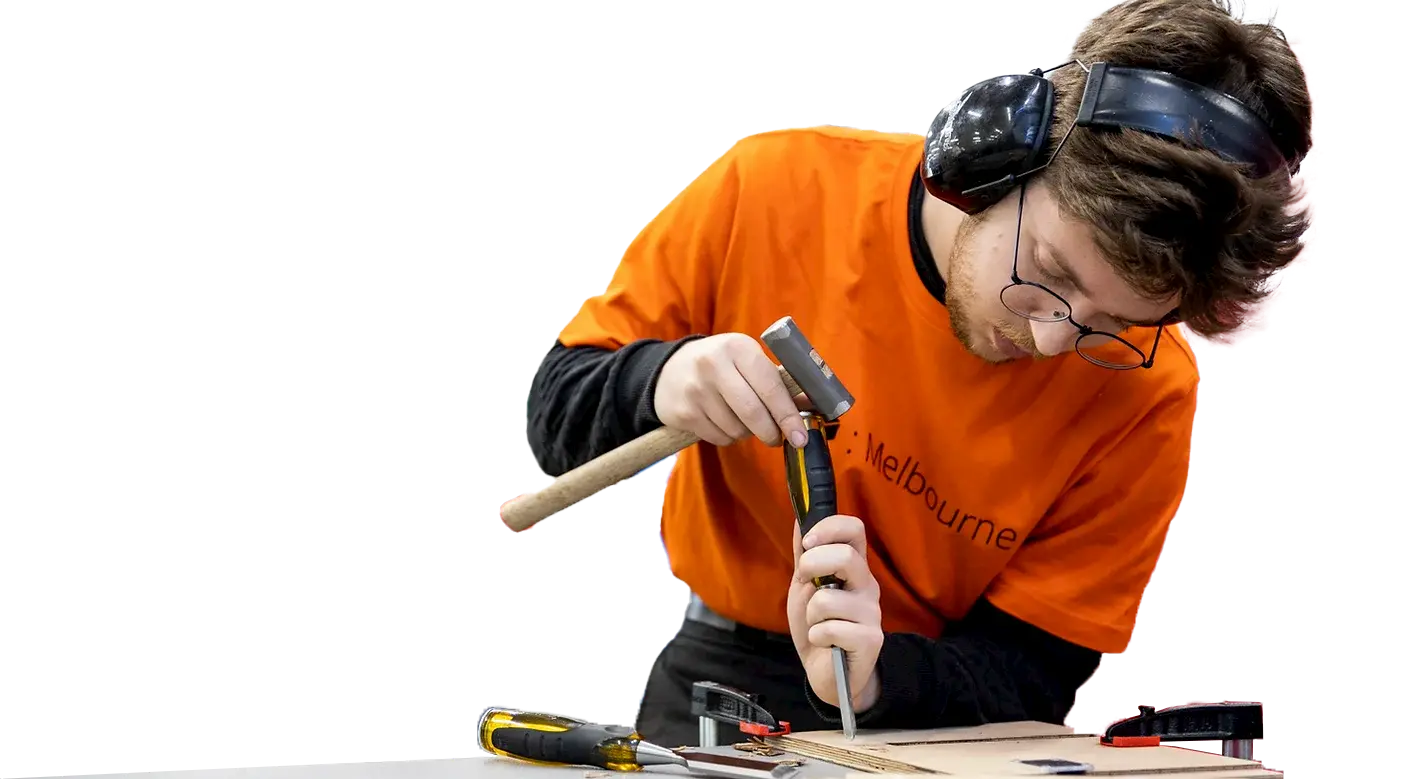Person in orange tom t-shirt using hammer and chisel on a piece of plywood.