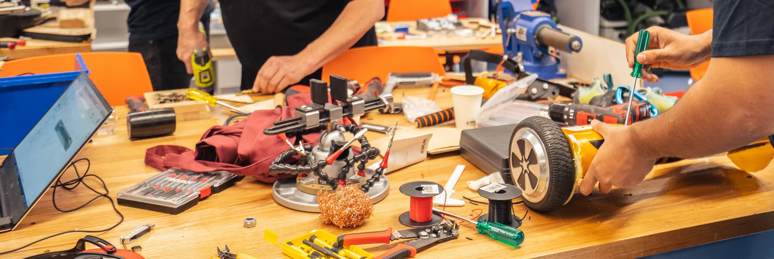 Workbench covered with electronics and hands of two people drilling and screwing.