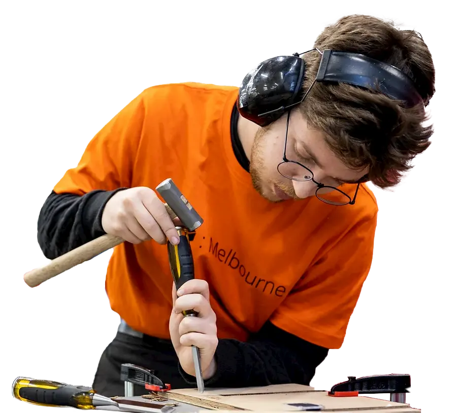 Man in orange TOM t-shirt using a hammer and chisel on a piece of plywood.