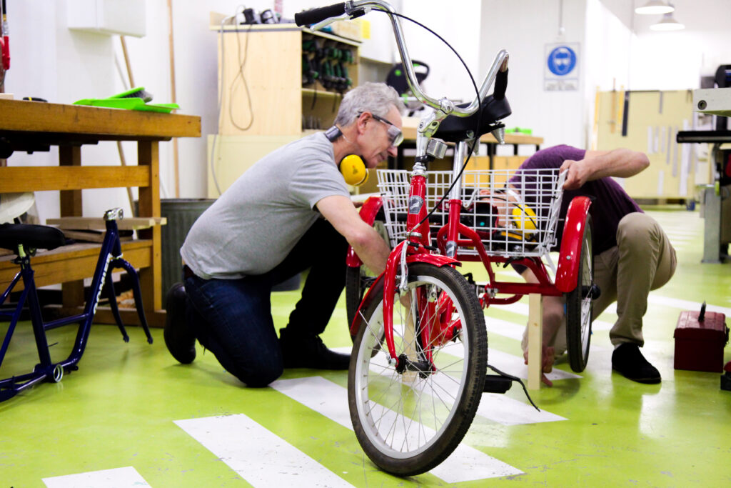 Two people are crouching on the floor working on a red tricycle.