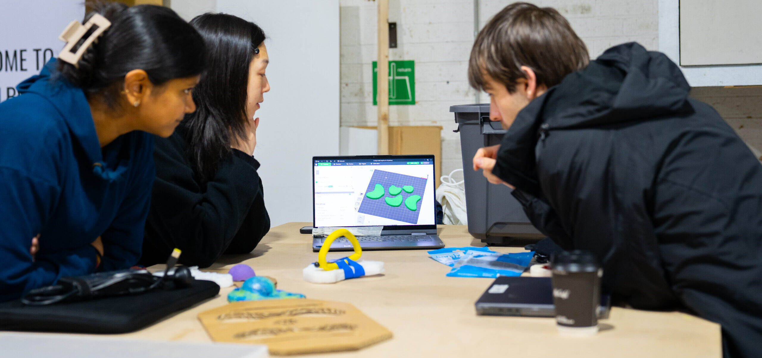 Three people leaning in to look at a 3d model on a computer.