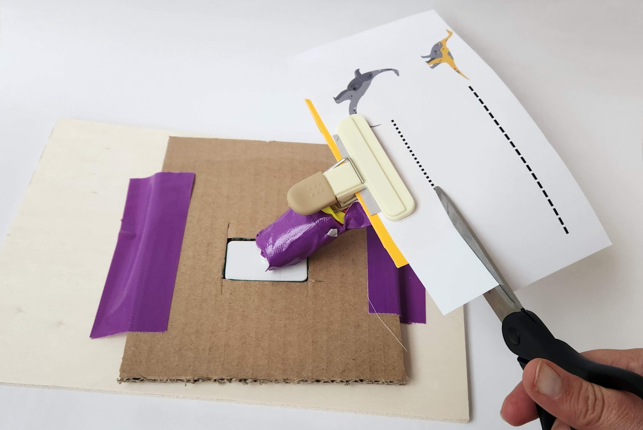 A cardboard base with a bulldog clip on a handle holding a piece of paper.