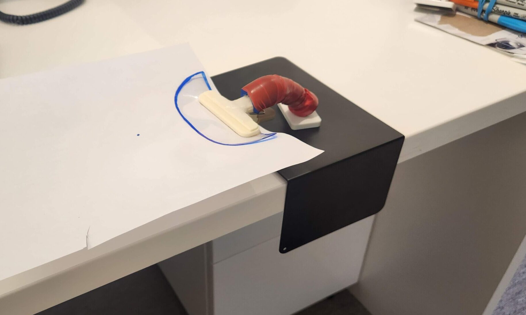 A black base board with a magnetic handle standing on top, using a bulldog clip to hold a piece of paper.