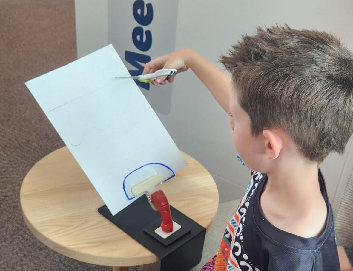 Boy sitting down and cutting a piece of paper with scissors.