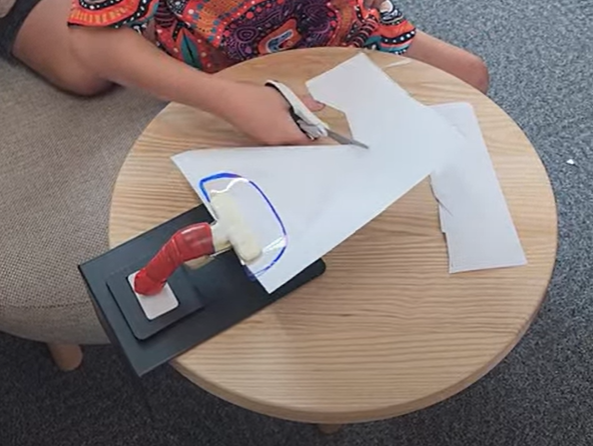 Boy using scissors to cut a piece of paper stabilised by the super gripper.