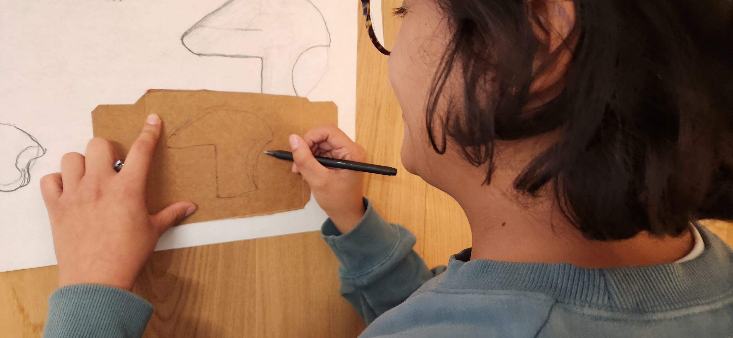 Back of womans head as she traces a shape on a piece of cardboard.