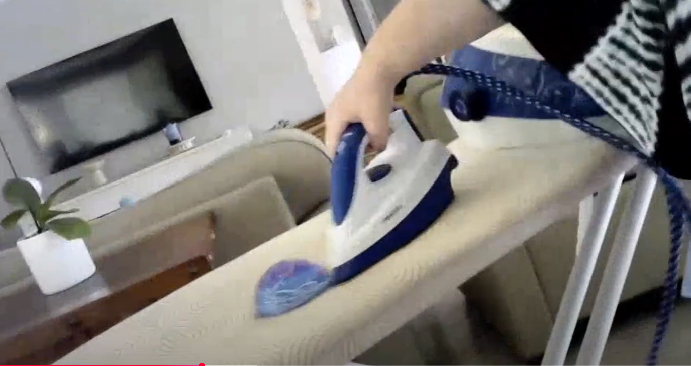 A hand holding an iron on an empty ironing board.