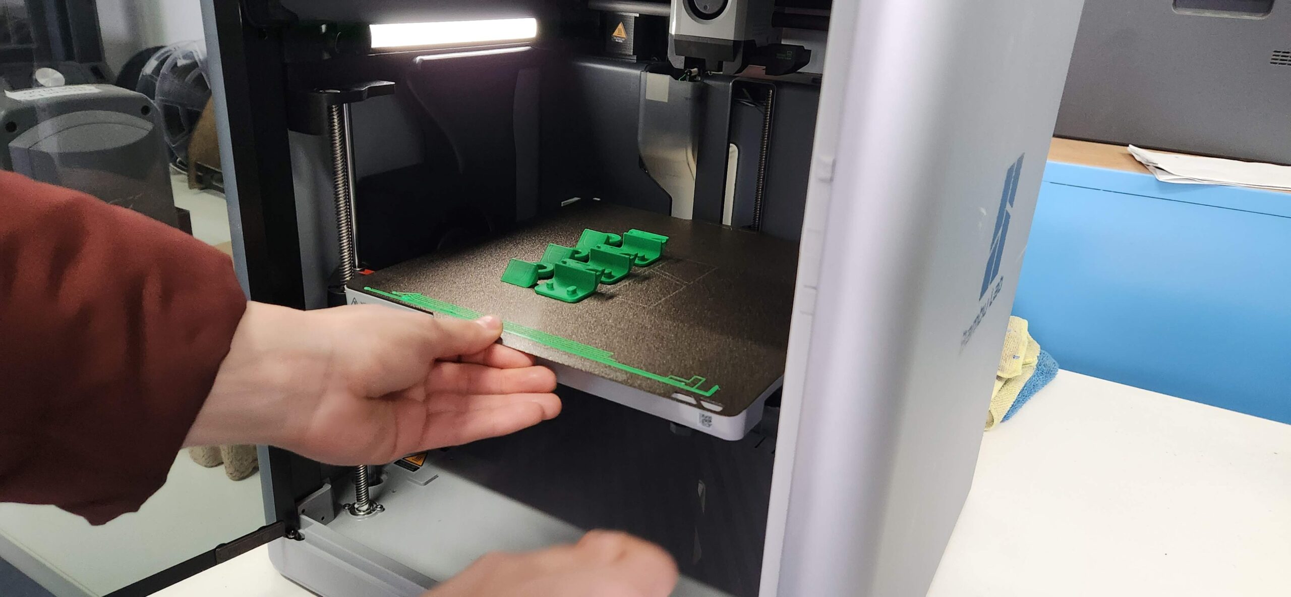 A hand is pulling out a sheet of 3d printed parts out of a 3d printer.